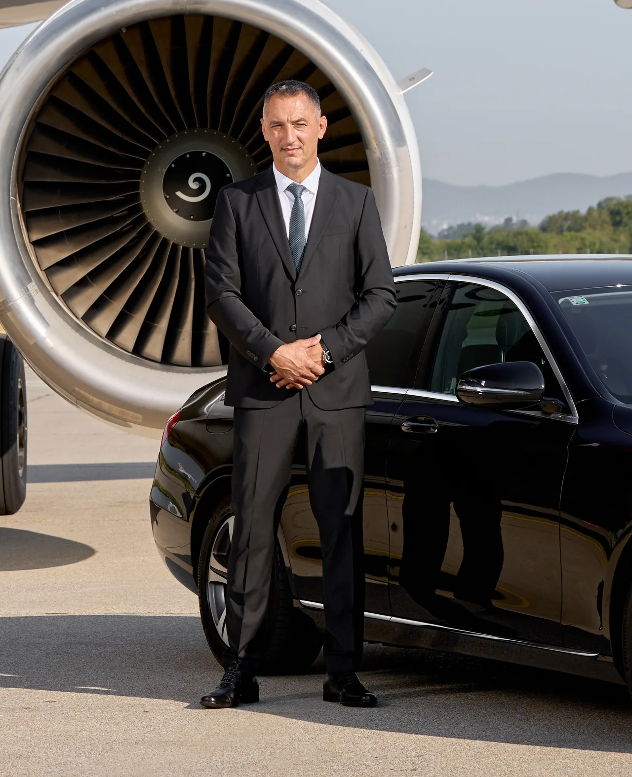 Profesionalni vozač u odijelu uz crni Mercedes